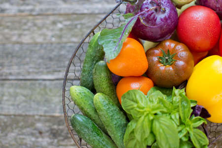 Metal basket with fresh vegetables on an old wooden background. Fresh peppers, tomatoes, cucumbers,...