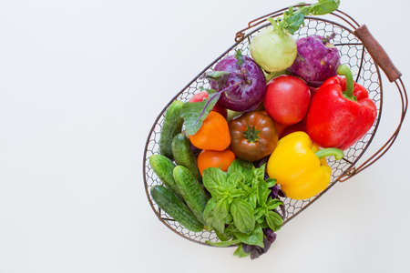 Metal basket with fresh vegetables on a white background. Fresh peppers, tomatoes, cucumbers, basil leaves and kohlrabi in metal basketの写真素材