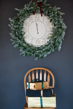Vintage Christmas clock with frame of Christmas wreath and gift boxes on a wooden chair on a black...