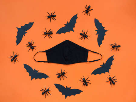 Black face mask and Halloween pattern with black decorations on an orange background. Black paper bat, ants and eyes, Halloween party decorations at pandemic coronavirusの写真素材