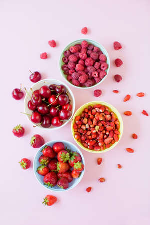 Strawberry, cherry, raspberry and small wild strawberry in colorful bowls on a pink background