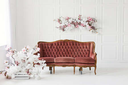 Vintage brown sofa and flowers wall decoration in light room with white wooden walls