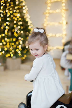 Cute little girl in a white dress near Christmas tree with decorations and lightsの写真素材