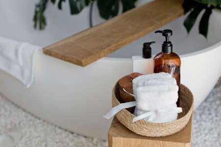 Stylish modern bathroom with body care products. Bottles, towel in a wicker basket near bathtubの写真素材