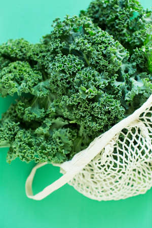 Green curly kale salad in white eco bag on a green backgroundの写真素材