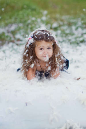 Feathers pillow mess and happy little girl outdoors in the fieldの写真素材
