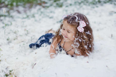 Feathers pillow mess and happy little girl outdoors in the fieldの写真素材
