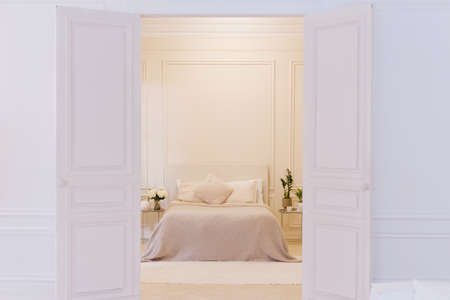Light bedroom with white walls, big bed, pillows and houseplants. Copy space, place for textの写真素材