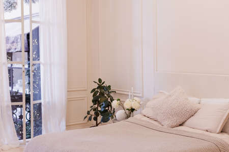 Light Christmas bedroom with white walls, big bed, pillows and houseplants and big window with winter Christmas viewの写真素材