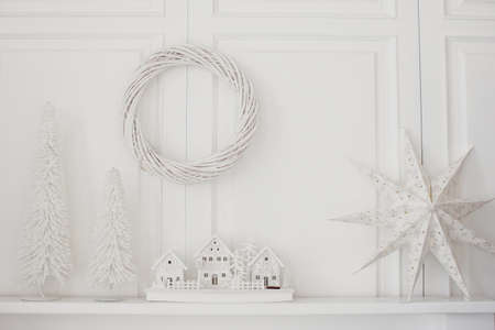 White Christmas decorations near white wall. White Christmas tree, wreath, Christmas wooden village and star.の写真素材