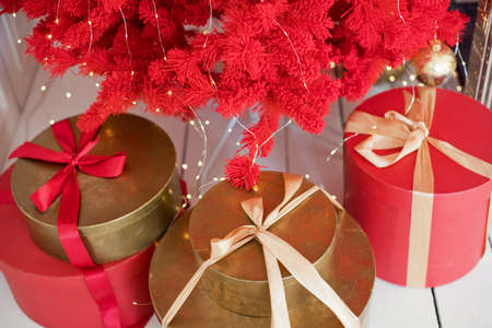 Red and golden Christmas gift boxes with ribbons near red Christmas treeの写真素材