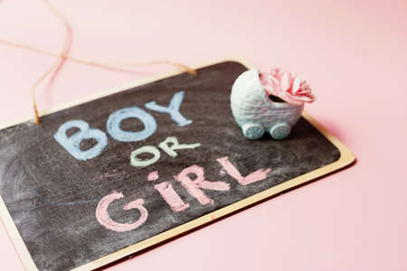 Chalkboard with sign BOY OR GIRL and blue pram vase with pink flowers. Gender reveal party with pink and blue decorations on a pink background. boy or girl partyの写真素材