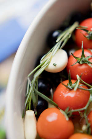 Tomatoes, garlic, olives and rosemary in baking form on a light background. Preparation for cooking...