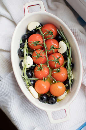 Tomatoes, garlic, olives and rosemary in baking form on a light background. Preparation for cooking a healthy dishの写真素材