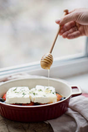 Baked feta cheese with tomatoes, olives, garlic, oil, honey and rosemary in baking dish on a rustic...