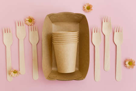 Paper brown disposable tableware. Paper cups, plates and wooden forks on pink background with copy spaceの写真素材