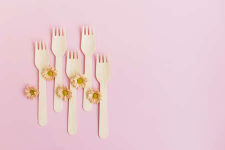 Disposable tableware, wooden forks and orange flowers on a pink background with copy spaceの写真素材