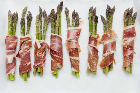 Asparagus with ham on white background. Tasty spring dish with asparagus and baconの写真素材