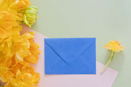 Envelope gift near flowers. Blue envelope, gift card or letter near bouquet of yellow tulip. Spring holiday concept, gift idea. Copy space, place for textの写真素材