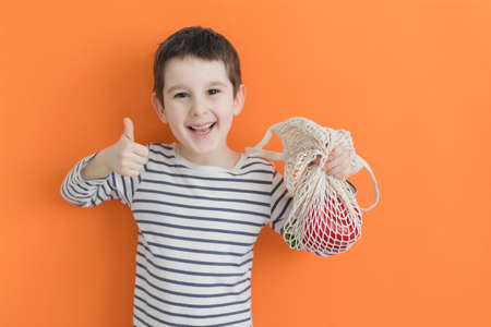 Child holds eco bag with fresh vegetables from farm market on an orange background with copy space. Healthy food concept, fresh vegetables, farm marketの写真素材