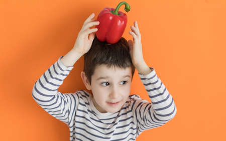 Child with vegetable red pepper on an orange background with copy space. Healthy food concept, fresh vegetables, farm marketの写真素材