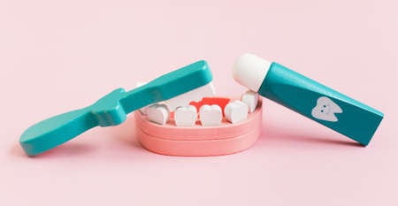 Dental background with wooden toy jaw, teeth, toothbrush and paste tube on a pink background....