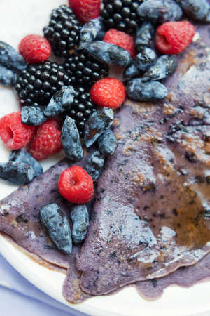 Purple crepes with berries and syrup on a white plate. Summer breakfast with crepes pancakes,...