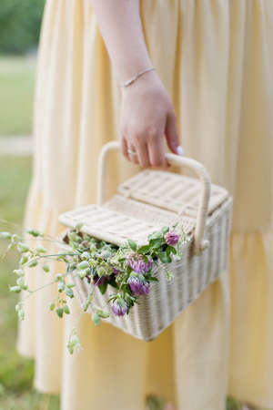 Caucasian woman in yellow dress holds light brown wicker basket with wildflowers.の写真素材