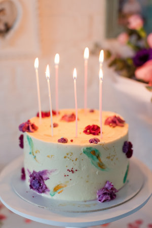 Birthday cake with burning candles on the white cake stand near beautiful bouquet of flowers. happy birthday gift conceptの写真素材