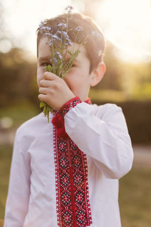 Caucasian boy in traditional ukrainian cloth vyshyvanka at the blossom garden holds dandelion....