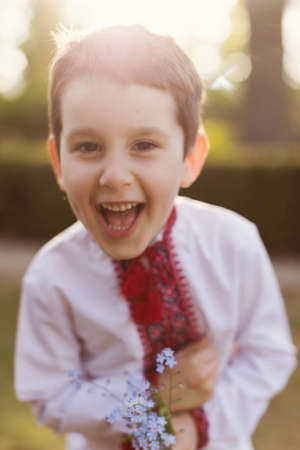 Caucasian boy in traditional ukrainian cloth vyshyvanka at the blossom garden holds dandelion. Ukraine ethnic costume, kid wear patriotic clothの写真素材