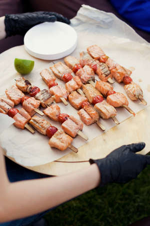 Grill salmon skewers on a tray. Woman holds plate with fish skewers and slice of limeの写真素材