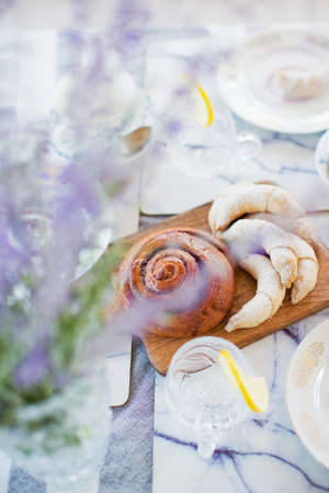Pastry loaf, small croissant cookies on a woodan desk and glasses with lemon slices at the table