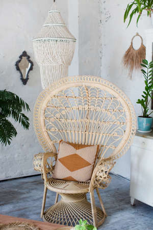Bohemian stylish interior with peacock armchair, green plants in flowerpots and vintage boho details