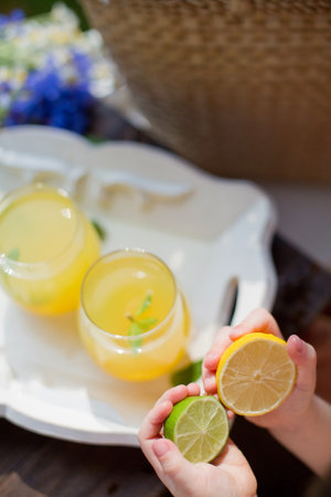 Glasses with lemonade with mint, lime, lemons and orange on a white wooden tray near straw bag with wildflowers. Summer drinks concept. Child holds lime and lemon slicesの写真素材