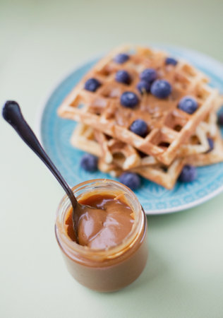 Belgian waffles with caramel sauce and blueberries on a light green background. Tasty homemade breakfast conceptの写真素材
