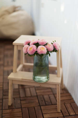 Beautiful bouquet with pink chrysanthemums aster flowers in green vase on a wooden ladder stoolの写真素材