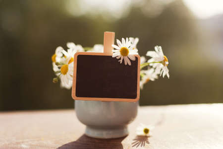 Small chalkboard copy space and bouquet of chamomiles in blue vase