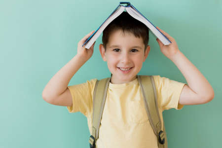 Caucasian preschool boy with school backpack holds book on a light green background with copy spaceの写真素材