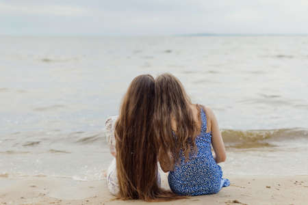 Two caucasian women with dark long hair sitting on the sand and looking on sea. Friend an girlfriends conceptの写真素材
