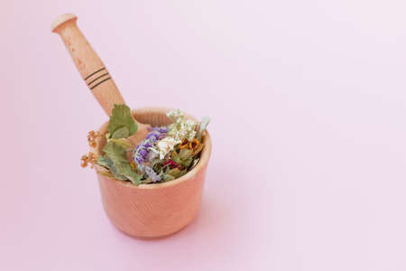 Homeopathy and herbal medicine concept. Wooden mortar and pestle with dry herbs on a pink background with copy spaceの写真素材
