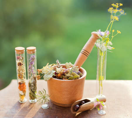 Homeopathy and herbal medicine concept. Wooden mortar and pestle with dry herbs, wildflowers and glass bottles on a wooden boardの写真素材