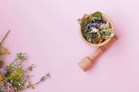 Homeopathy and herbal medicine concept. Bouquet of wildflowers and wooden mortar and pestle with dry herbs on a pink background with copy spaceの写真素材