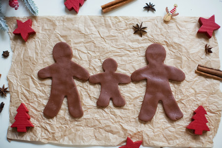 Gingerbread man family on baking paper background with cinnamon sticks and star anise. Making...