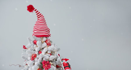 Christmas tree with striped knit hat, red decorations and toy santa. Banner with Christmas tree,...