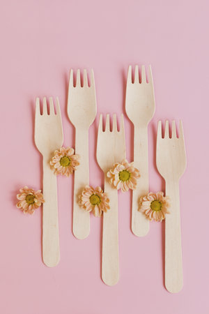 Disposable tableware, wooden forks and orange flowers on a pink backgroundの写真素材