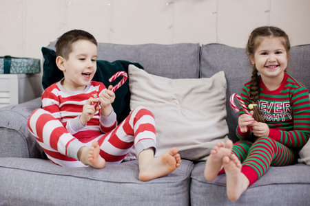 Preschool boy and girl in Christmas pyjamas sitting on a grey sofaの写真素材