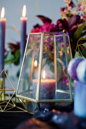 Burning candle in glass vase near flower composition with pink and blue flowersの写真素材