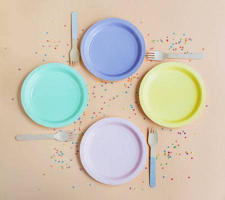 Party table setting with empty colorful plates on a beige background with confetti,copy spaceの写真素材