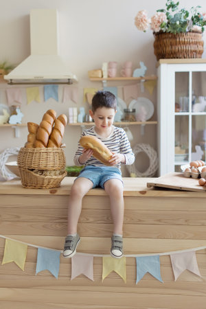 Caucasian boy with baguettes on a light kitchen interior with Easter decorationsの写真素材